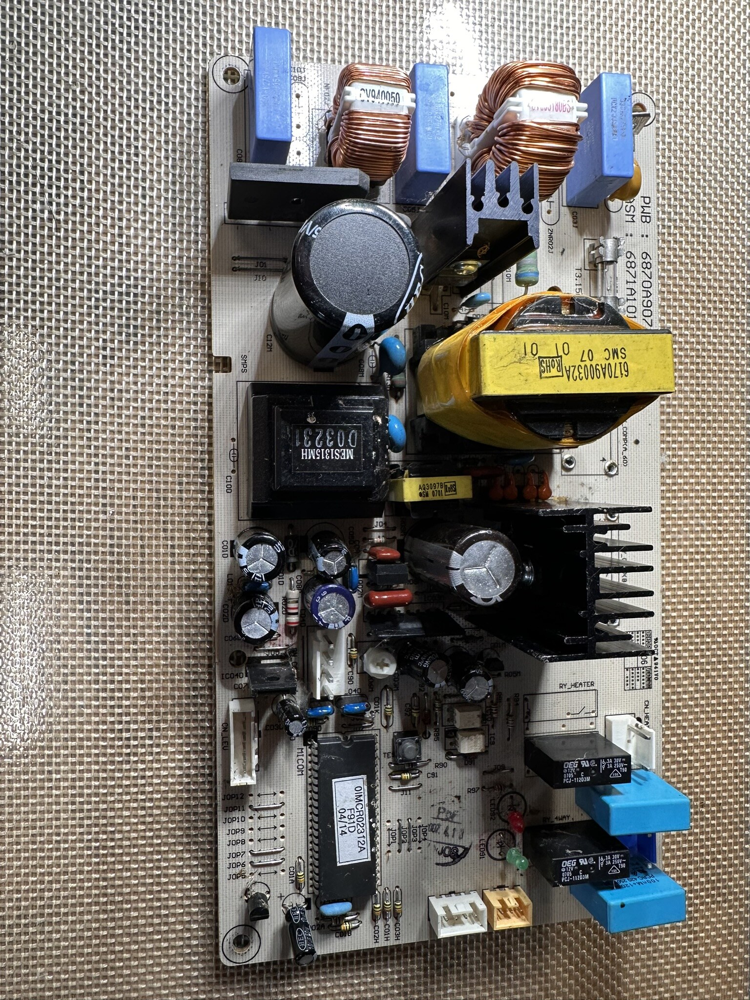 Appliance control board with relays, transformer, capacitors, and connectors on a repair bench